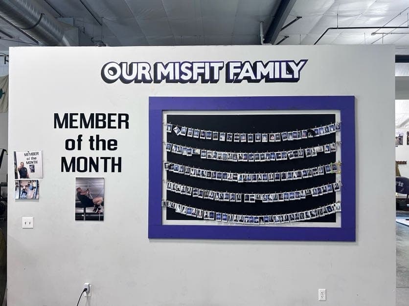 The Our Misfit Family wall: rows of Polaroid member portraits beside a Member of the Month display
