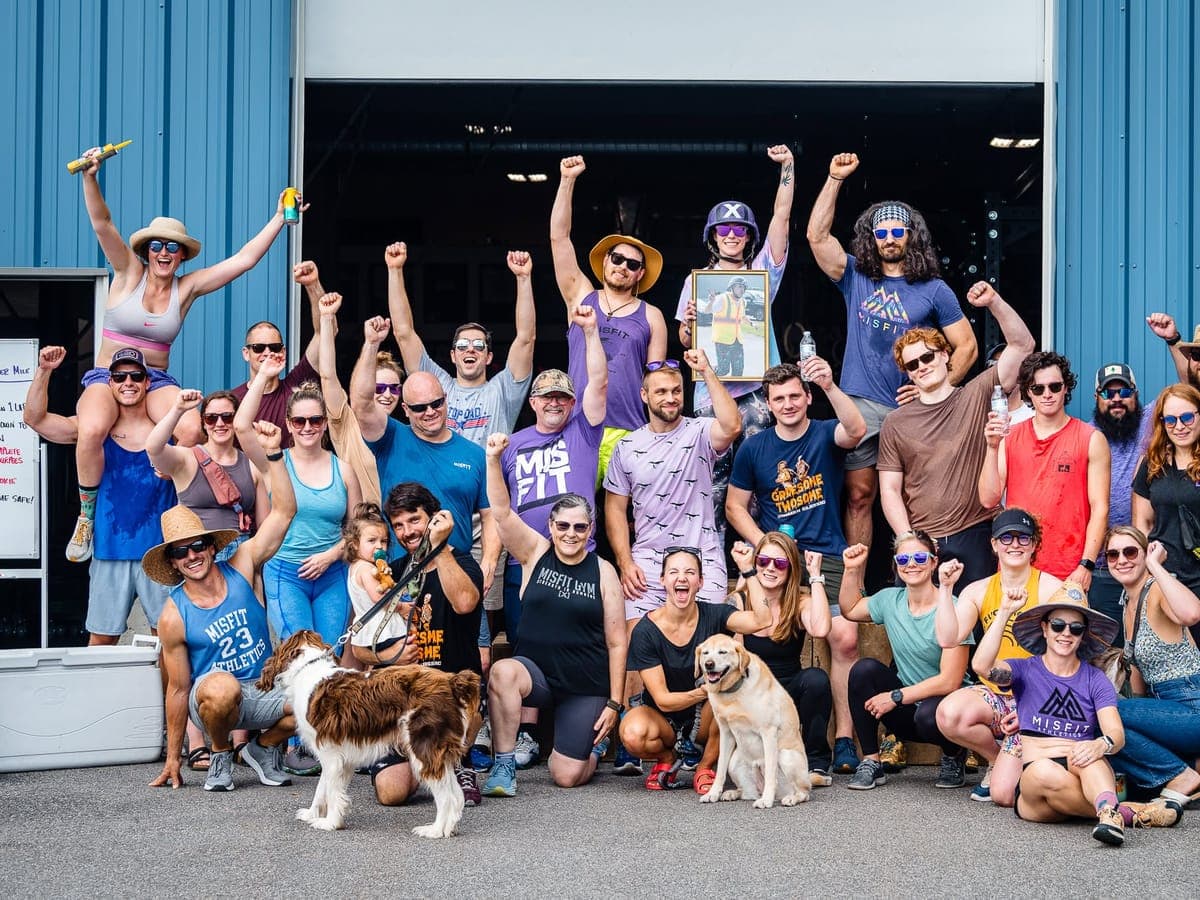 A big group of members and two dogs posing with fists in the air outside the gym's open bay door