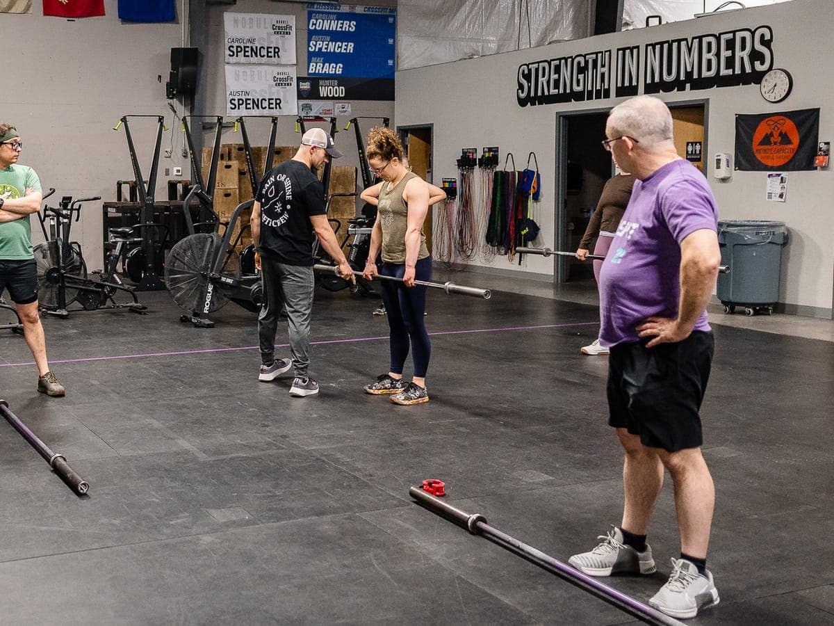 A coach adjusting a member's grip on an empty barbell while two other members watch