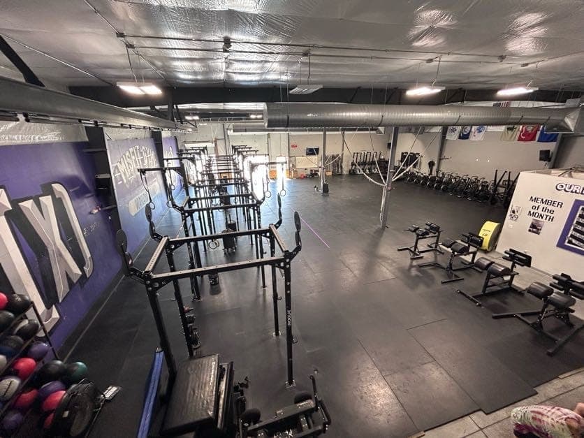 The main floor from above: rigs and squat racks under the purple mural, open platforms beyond
