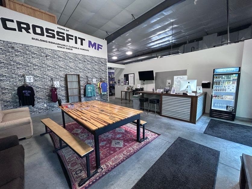 The lobby: wall sign, long communal table, front desk, and the honor-system store's shirt rack