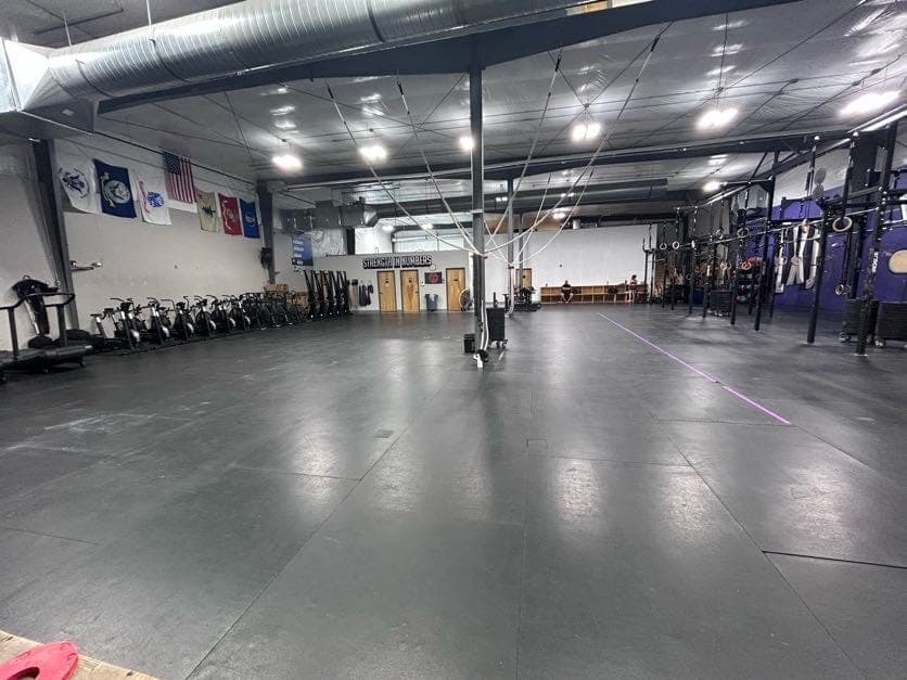 Main floor at standing height: rig and rings to the right, cardio row to the left, open mats between