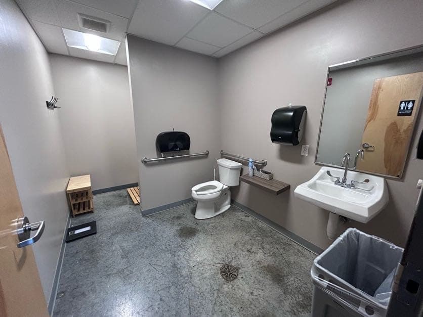 One of the restrooms: sink and mirror, grab bars either side of the toilet, and a wooden bench