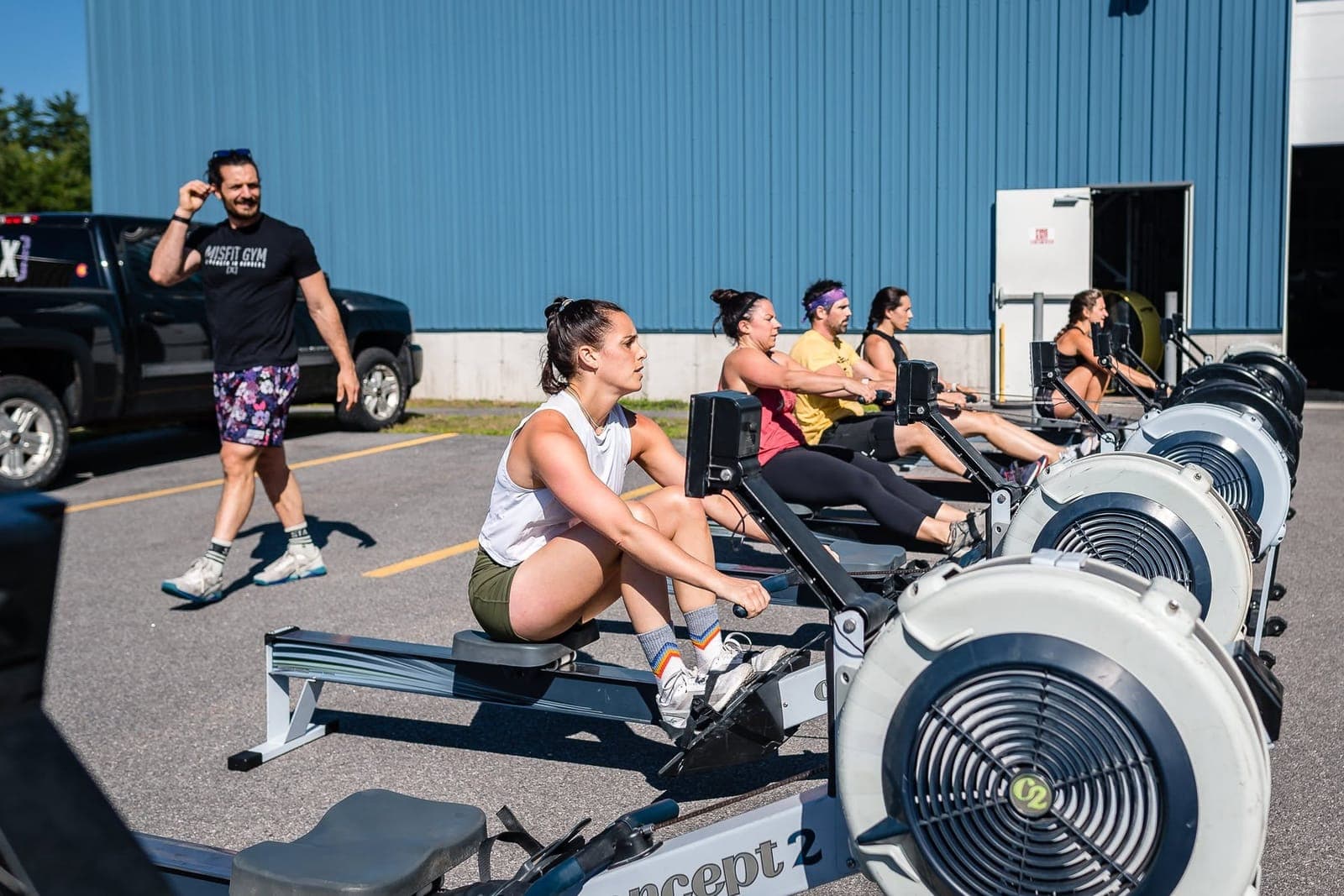 Five Misfit members rowing in a line on Concept2 ergs in the sunny parking lot outside the gym